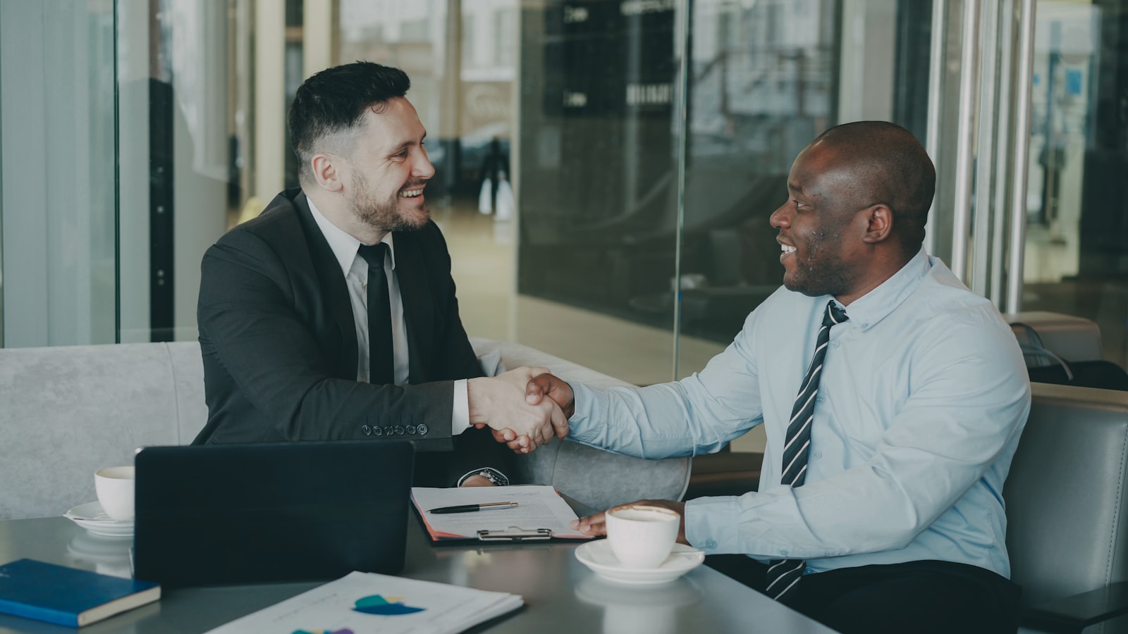 Two businesspeople shaking hands across a deal table